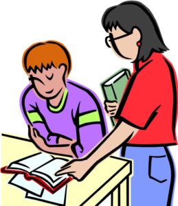 Teacher in red shirt standing by student seated at a desk helping the student