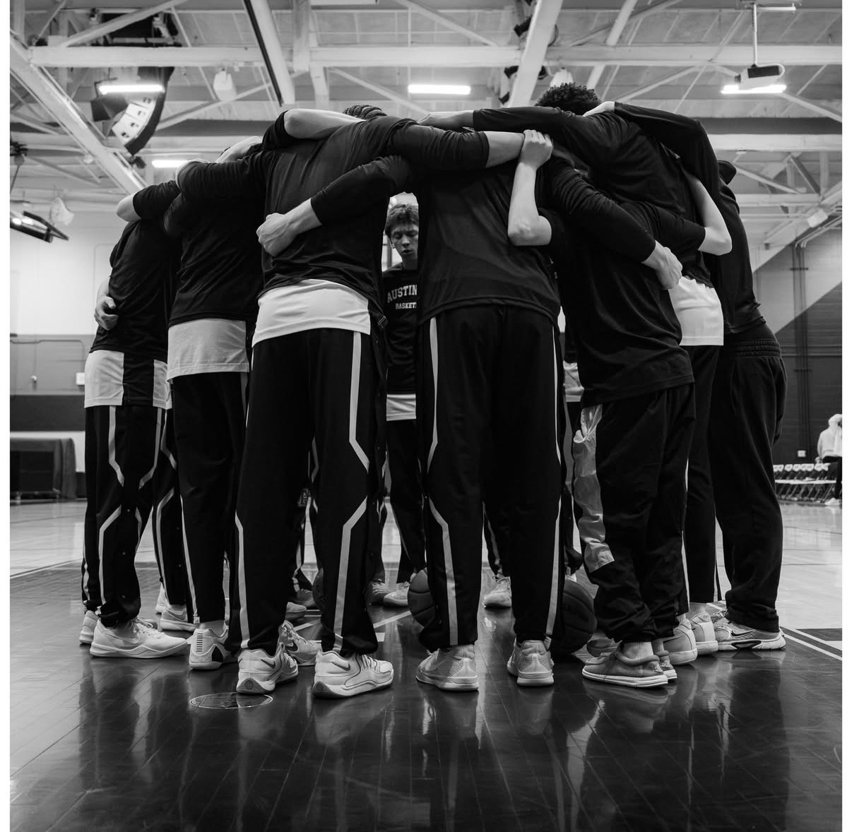 Photo of the AHS Boys basketball team huddled together before a game. The photo is black & white and of whole Maroons team.
