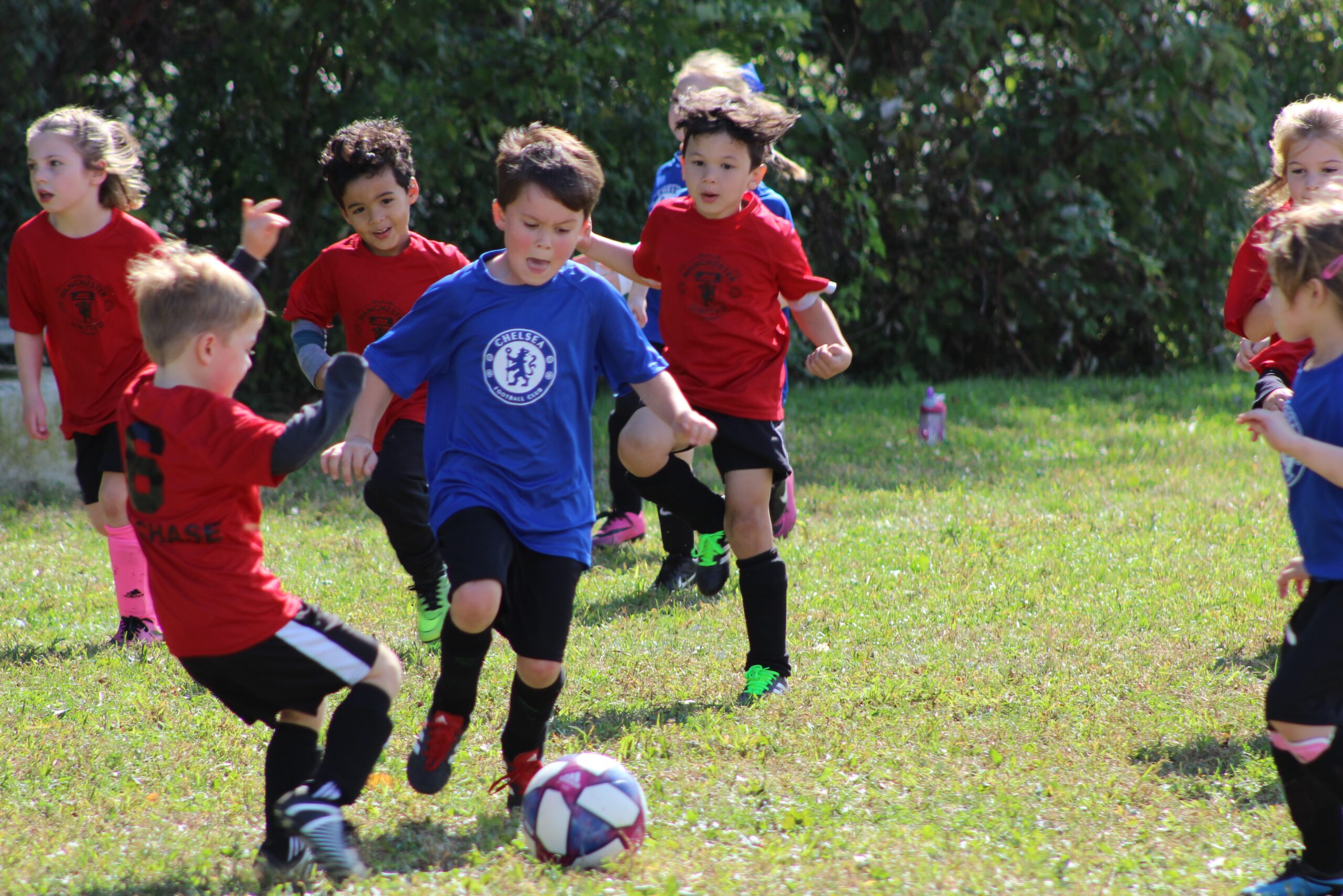 boy in red and blue soccer jersey kicking a ball on green grass field during daytime