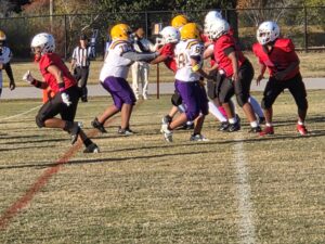 Football players in red/black and white/purple uniforms engaged in a play.