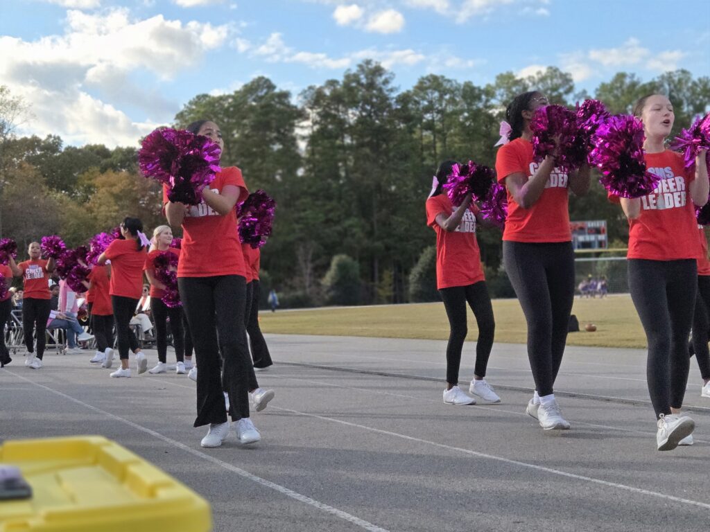 Cheerleaders in red shirts and white leggins with pink pom poms.
