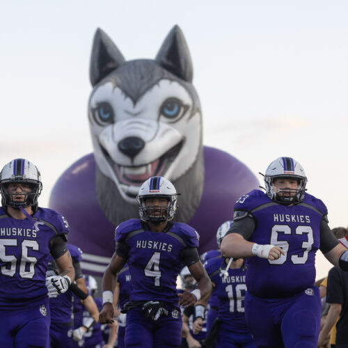 Football players running in front of a large inflatable husky