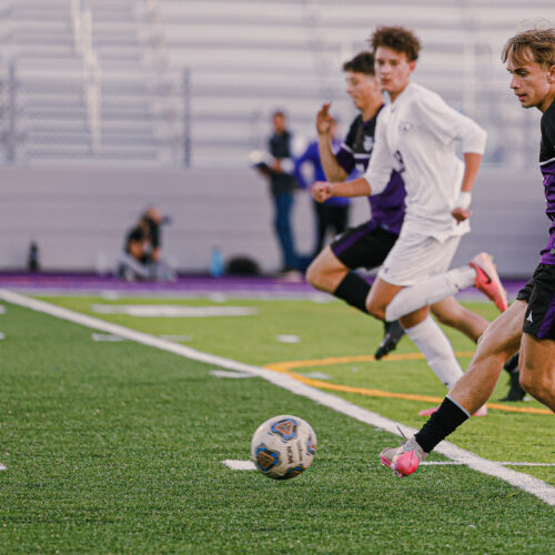 3 Soccer players run down a field behind a soccer ball