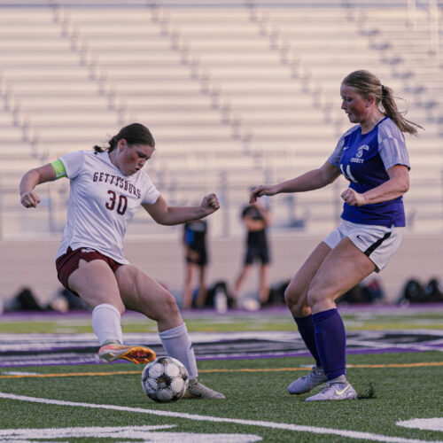 Two soccer players fight for the soccer ball on a field.