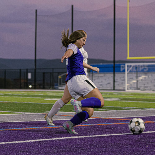 Two soccer players fight for the soccer ball on a partially purple field