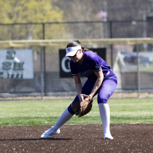 Softball player leans over to catch a low ball on a field