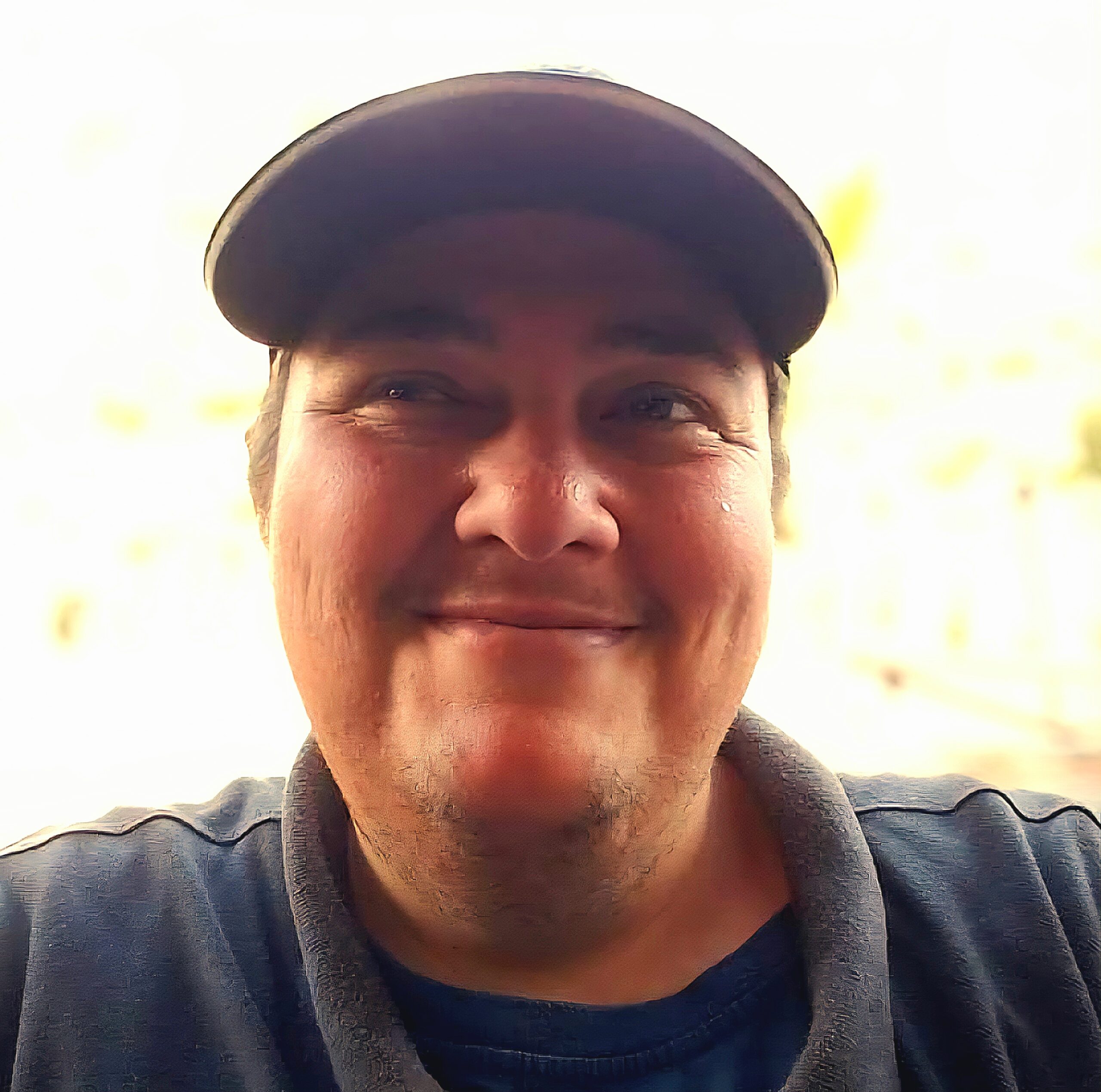 Headshot of a smiling man in a dark baseball cap and a blue shirt, looking slightly to the right.