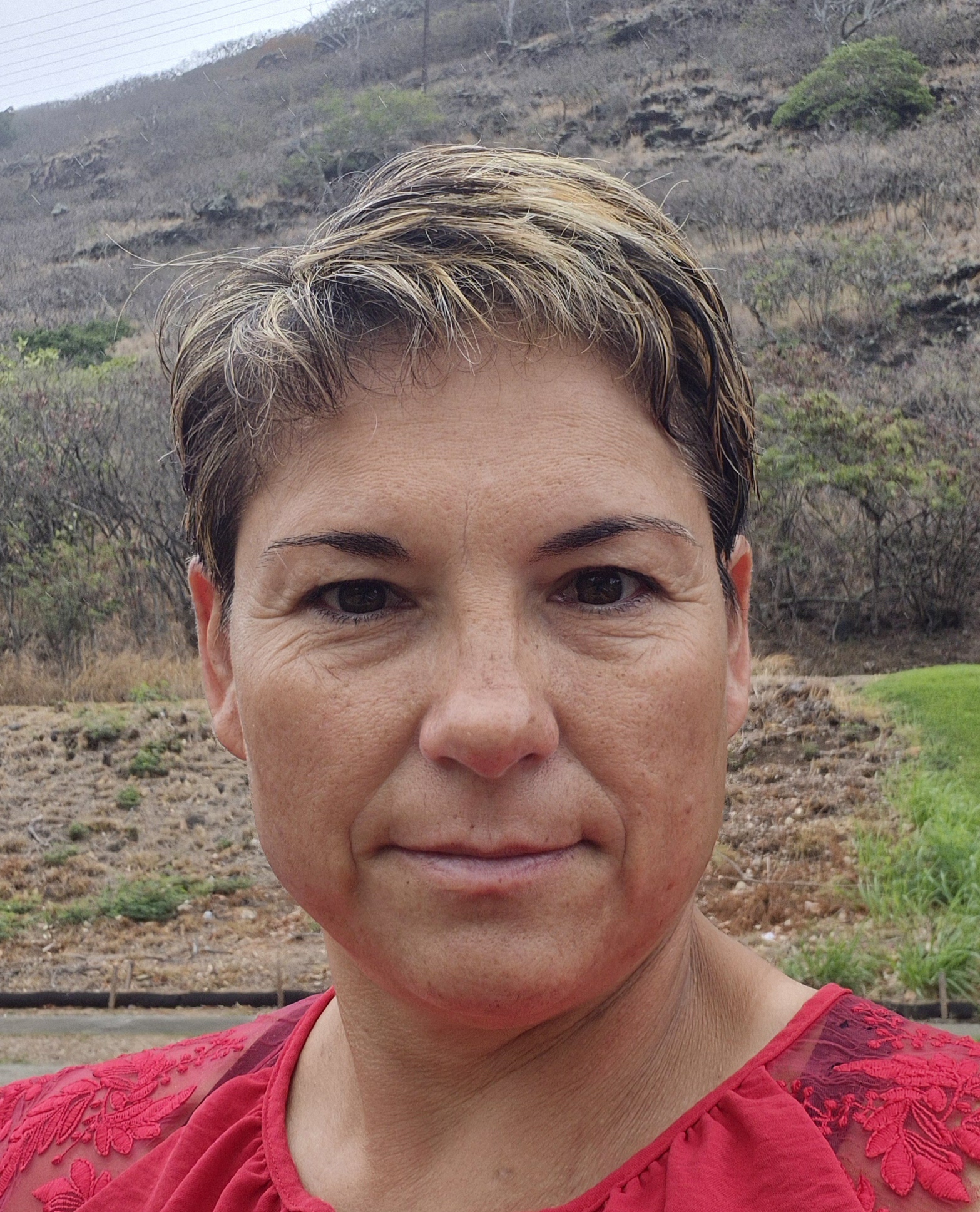 Headshot of Coach Victoria Ruelas, a woman with short, light brown hair, wearing a red top, with a hillside in the background.
