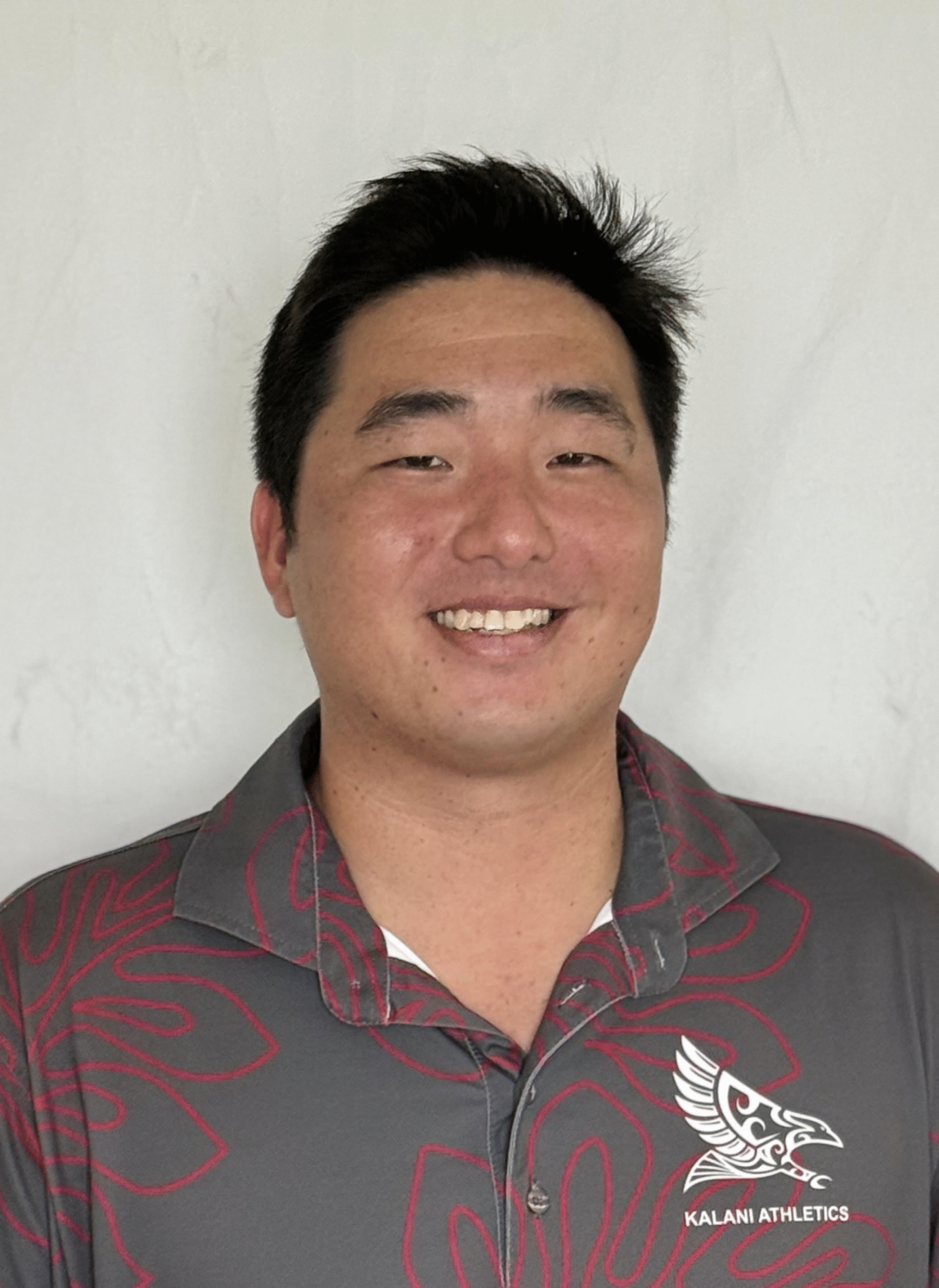 Headshot of Coach Devin Lee smiling, wearing a gray polo shirt with red designs and a Kalani Athletics logo