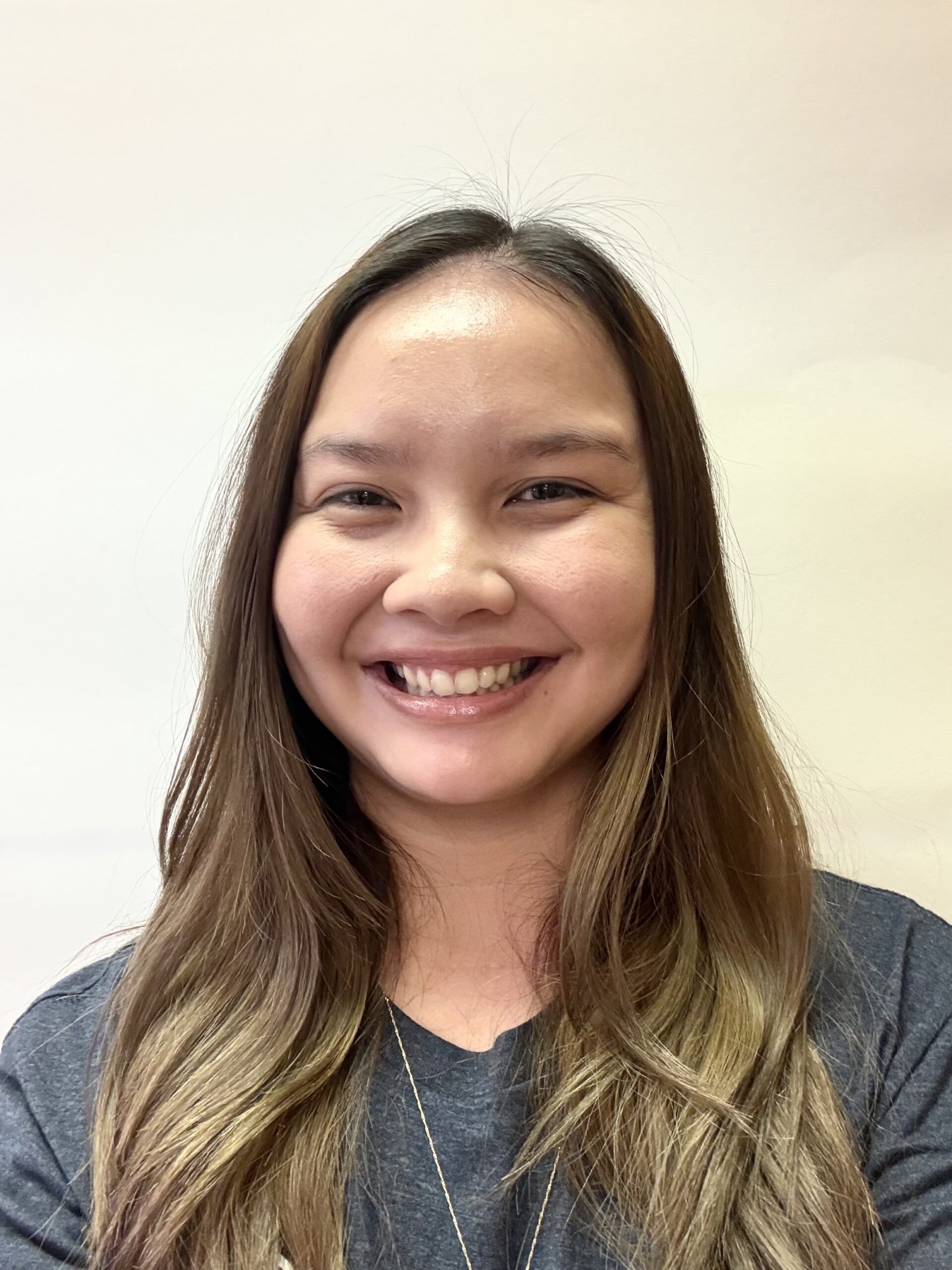 Headshot of a smiling woman, Coach Sarina Lee, with long brown hair, wearing a dark shirt and a silver necklace