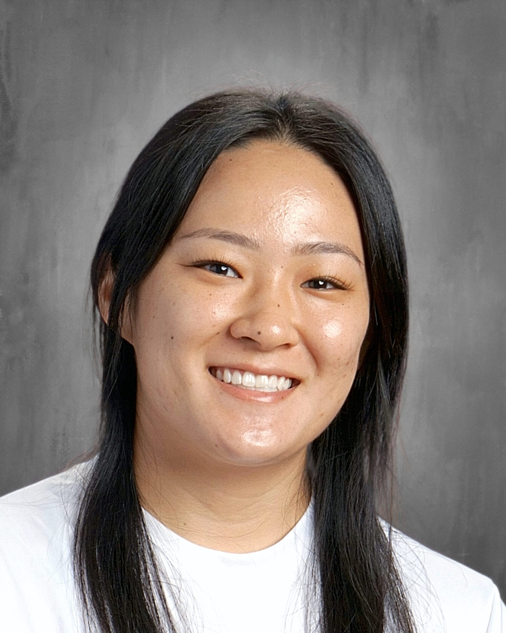 Headshot of a smiling woman with long dark hair, wearing a white t-shirt against a gray background