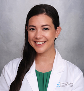 headshot of Dr Courtney Taum, woman with long dark hair wearing a green top under a white doctors coat