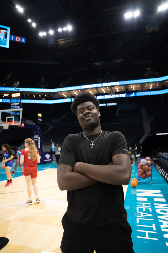 Boy posing for photo with basketball p[layers in the background.