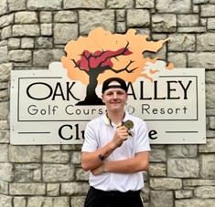 One male golfer standing in front of a stone wall at Oakv Valley golf course results holding his championship medal.
