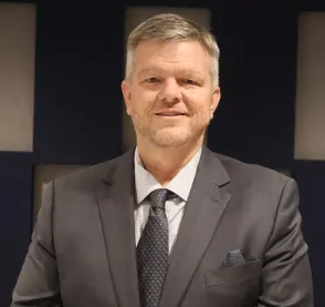 Tom Harper is suit and tie smiling