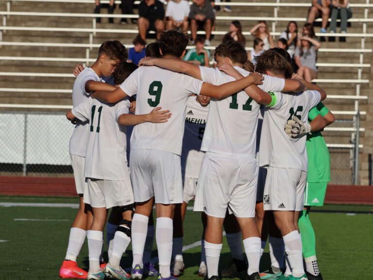 soccer players in a huddle after scoring a goal wearing white uniforms