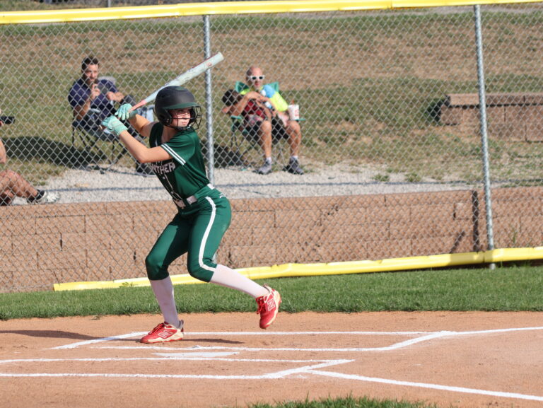 Softball player at bat wearing a green uniform