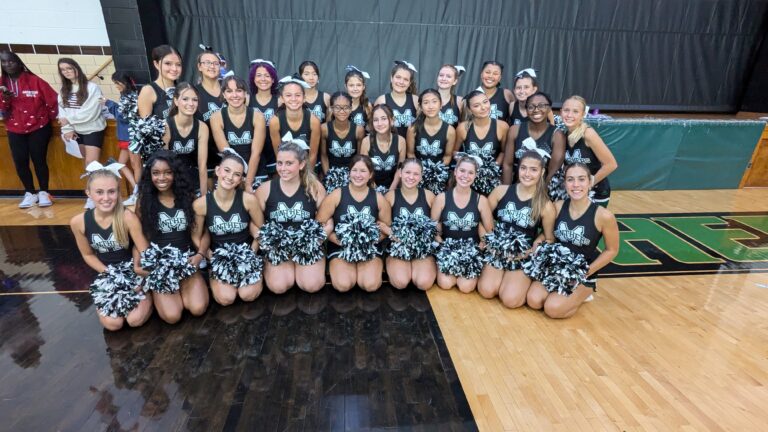 Group of cheerleaders smiling after a performance. wearing black uniforms and holding poms