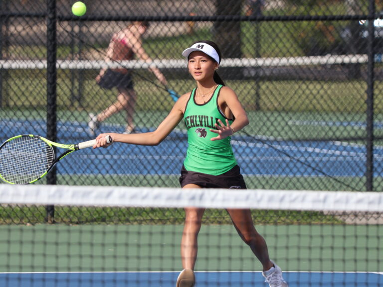 Girl tennis player in green mehlville uniform swinging at ball with tennis racquet