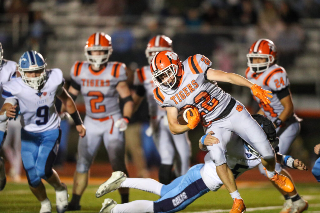 A football player from Elkins runs the ball while being tackled by a player.