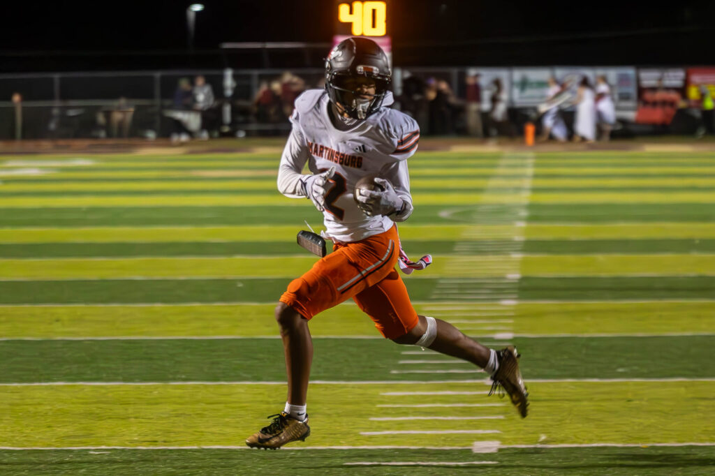 A football player in a white jersey with orange pants and a black helmet runs with the ball.