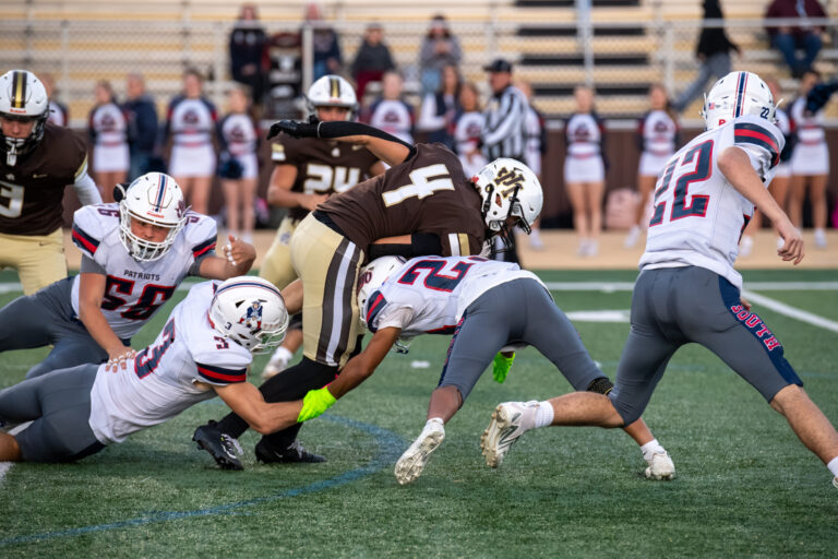 A player wearing a brown jersey getting tackled by two players.