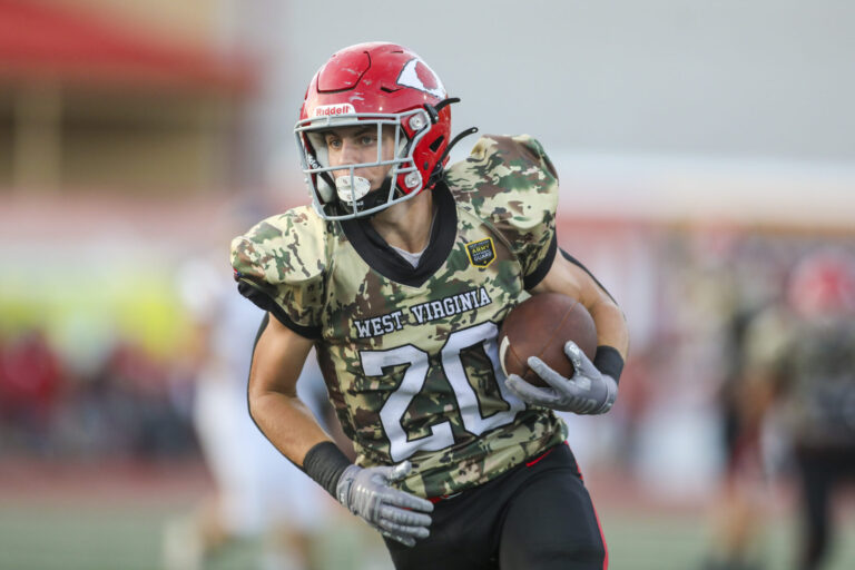 A player with a red helmet and camaflouge jersey runs with the football.