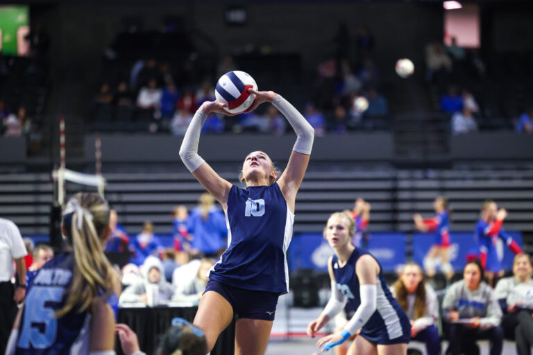 A volleyball player sets a pass for a teammate in a large arena.