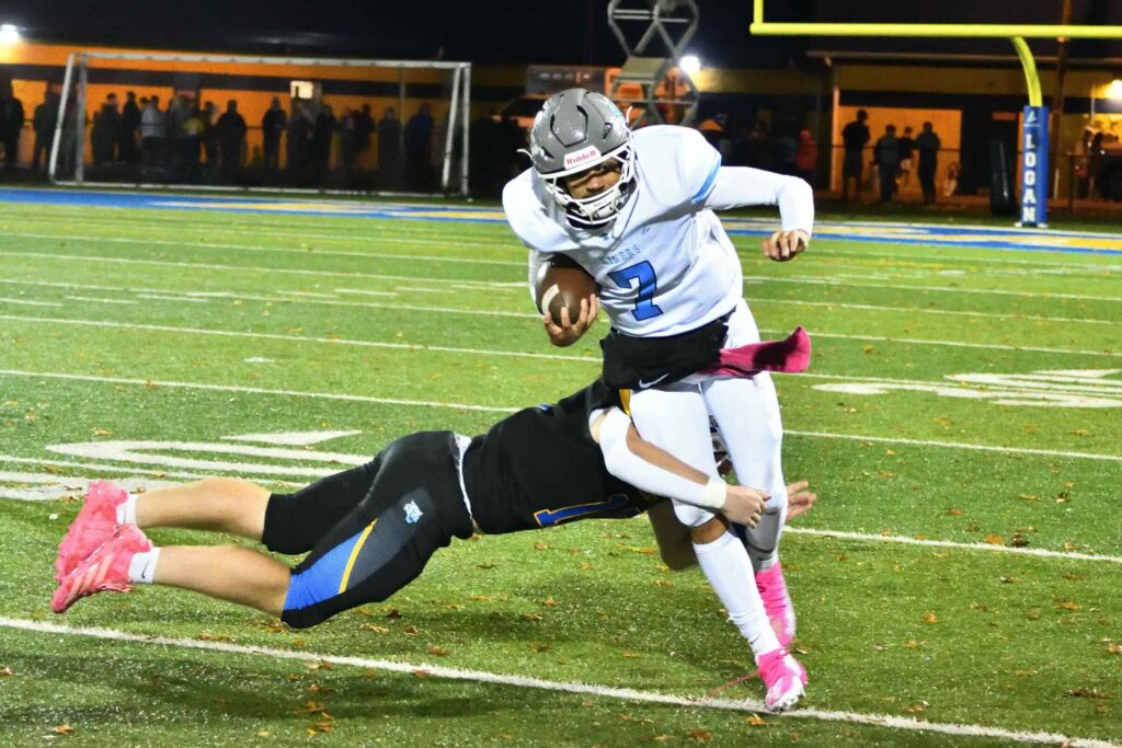A ball carrier in a white No. 7 jersey and pink cleats breaks a diving tackle attempt from a defender in a black jersey during a night football game.