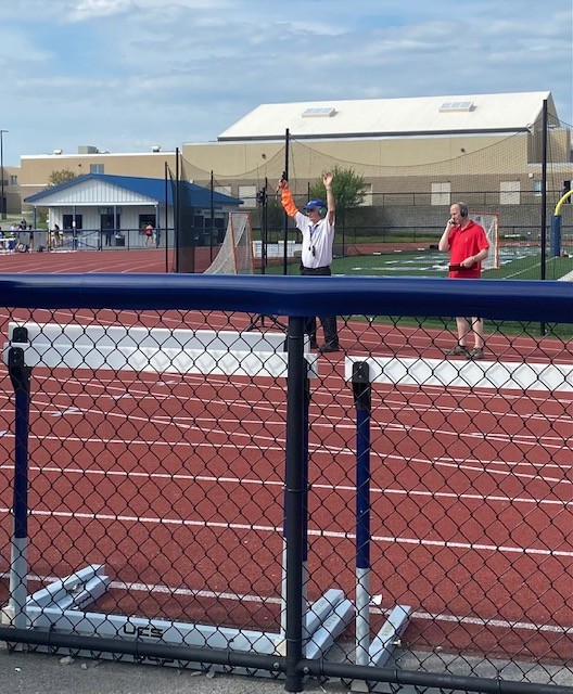 Adult male holding hands up on an outdoor track beside another adult male