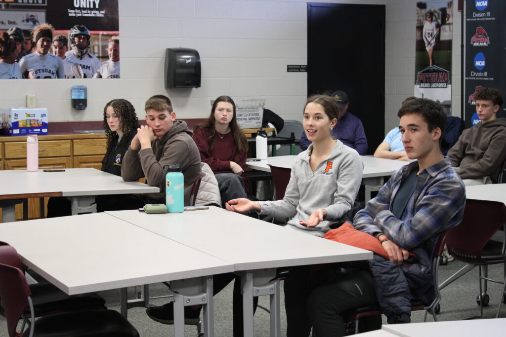 Small group of high school students sitting at desks listening and participating in discussions
