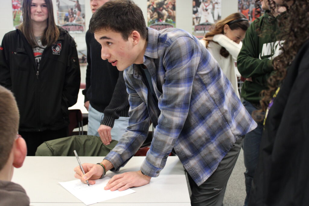 Male high school student with a pen and piece of paper in hand