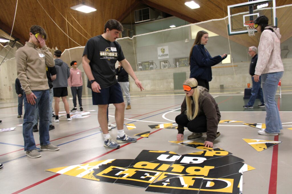 Small group of young students blindfolded and some not blindfolded working together to solve a puzzle