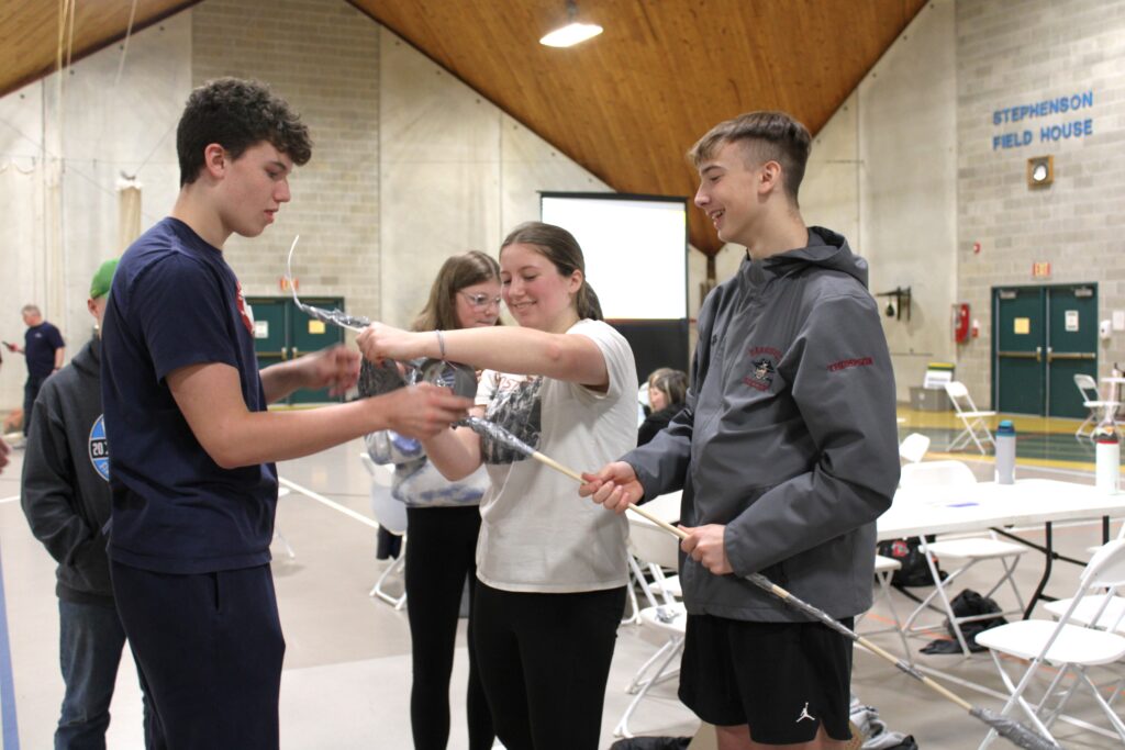 Two male and a female student holding a long pole working together to complete a project