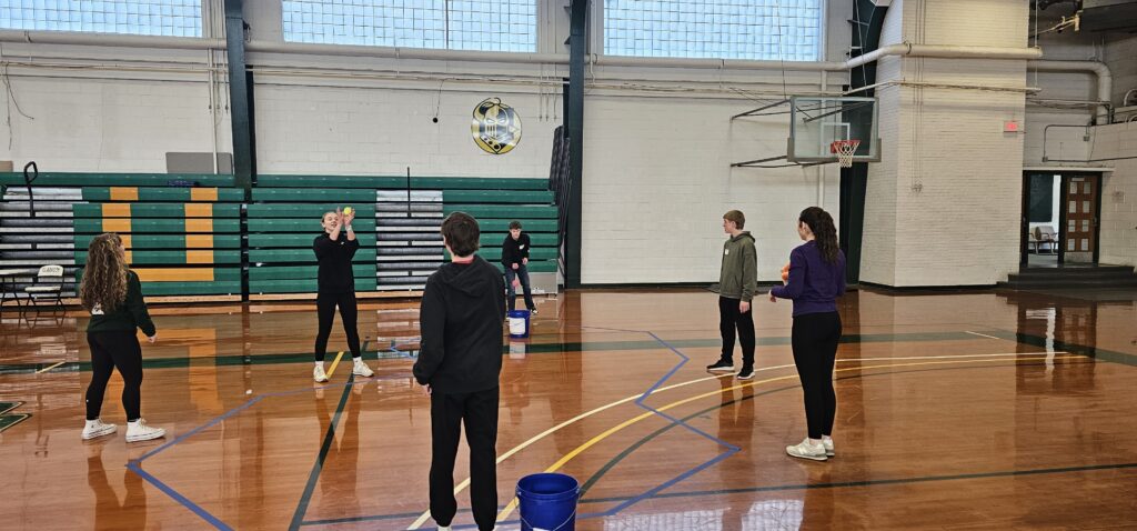 Small group of students standing and gathered in a circle throwing objects to each other