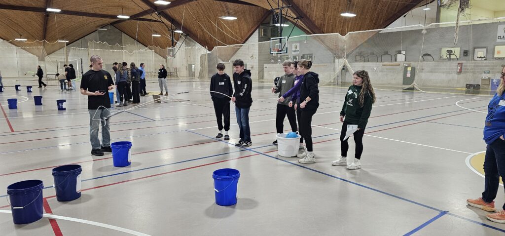 Small group of students using a pole to place objects in buckets