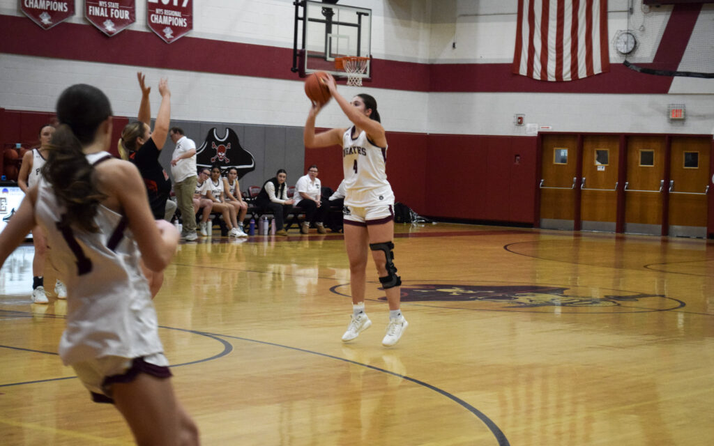 Female high school student wearing a white and black uniform on a basketball court during a game shooting the basketball