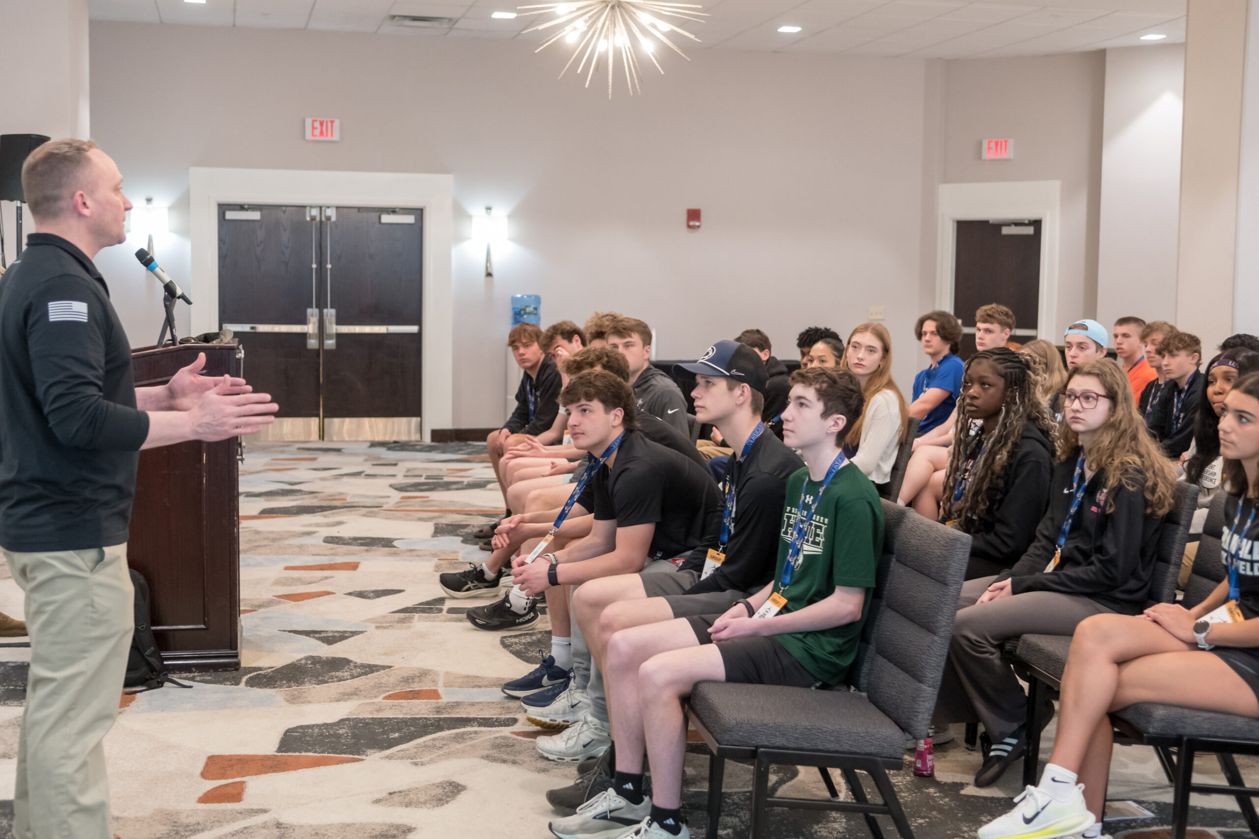 Large group of high school students seated in a conference room listening to an adult male give a presentation