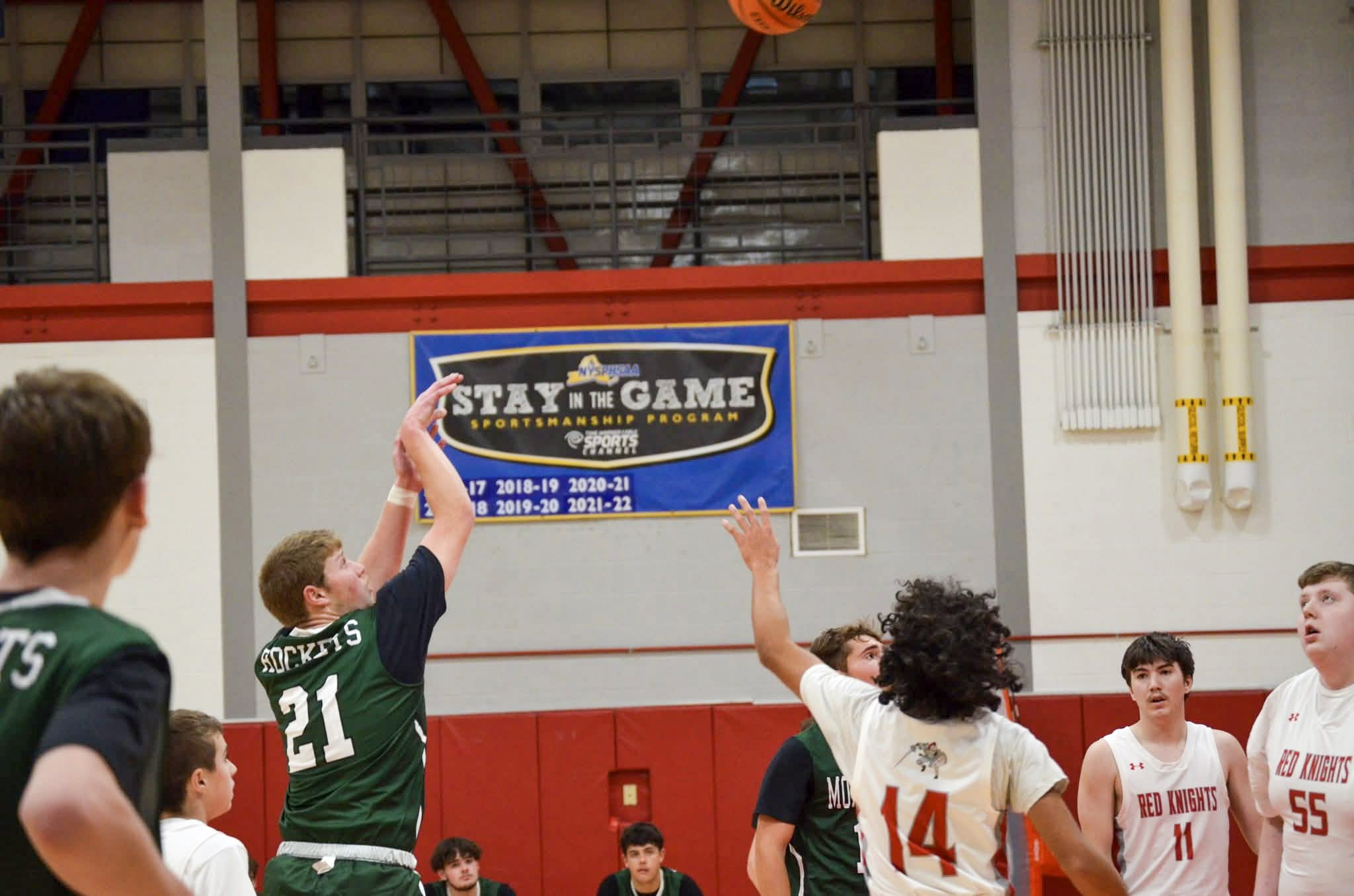 Male high school basketball players wearing green and white and white and red jerseys during a game