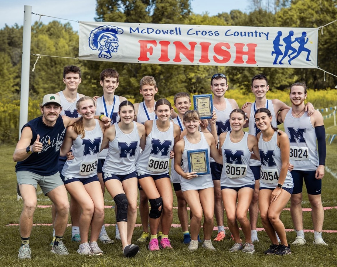 The McDowell Cross Country team posing together for a group photo under the finish line banner after winning first place at the McDowell Invitational.