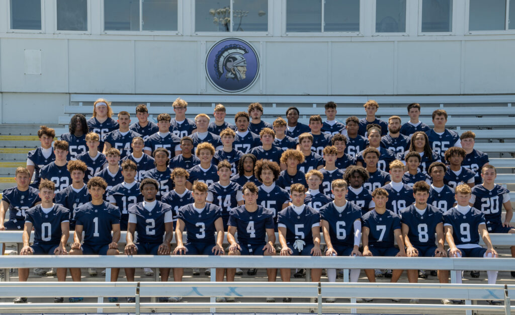 McDowell football team posing together in uniform on bleachers outside the school.