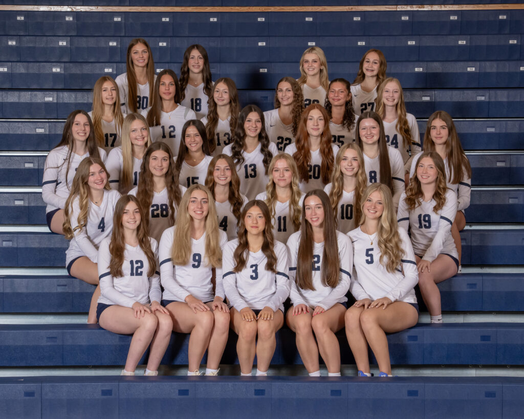 The McDowell girls varsity and JV volleyball team poses for a photo on the bleachers in the school gym.