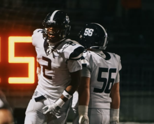 Two McDowell football players in a white jersey running in celebration.
