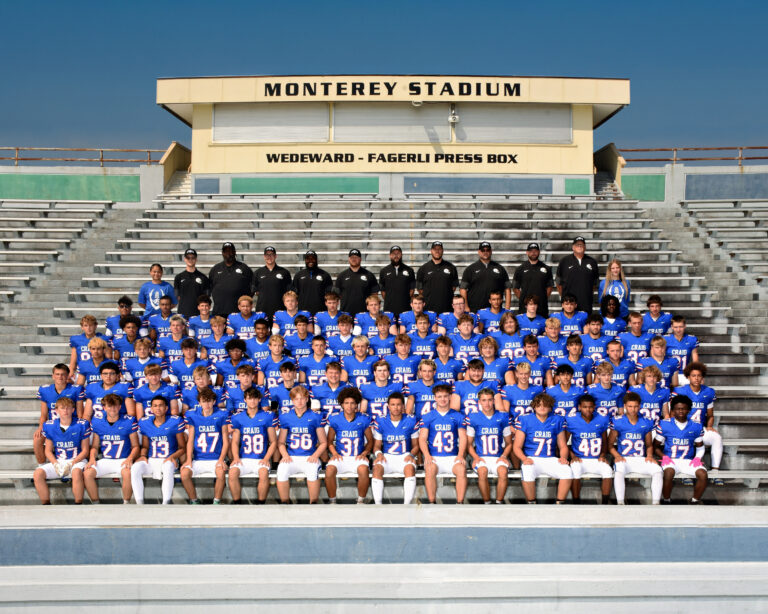 Varsity football team, athletes in blue uniforms sitting on benches at Monterey Stadium
